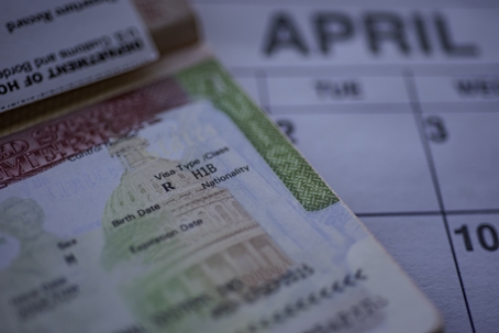 H1B visa (for specialty workers) stamp in passport, blurred april calendar on background. H1B visa program deadline concept. C