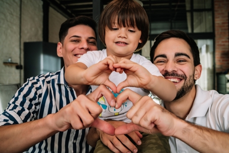 same-sex couple and adopted child making hearts with their hands