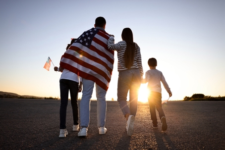 family with US flag on their shoulders walking towards the sunset
